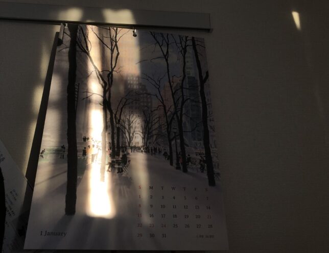 部屋の壁と、壁にかけてあるカレンダーに夕日があたっている。カレンダーはイ・キュテさんのイラストカレンダーで、2023年1月のもの。